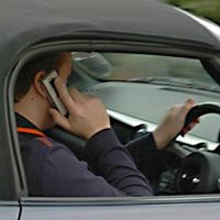Photo a driver holding a mobile phone to his head whilst holding the steering wheel rather than using a bluetooth kit